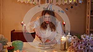 Upset woman cutting birthday cake with kitchen knife. A woman looks at the camera while holding a knife in her hand.