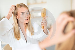 Upset woman examines and combats hair loss and flakes indoors