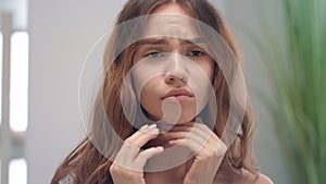 Upset woman feeling sore throat and touching skin neck front bathroom mirror