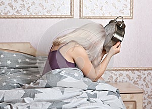 Upset woman, hanging his head, sitting with an alarm clock in the bedroom.