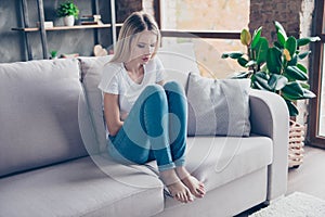 Upset woman has first symptoms of pms. She is sitting on a sofa