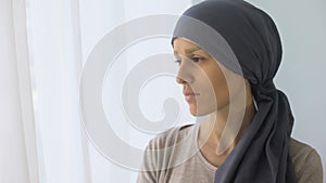 Upset woman in headscarf looking in window, rehabilitation centre, fatal disease