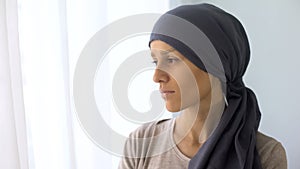 Upset woman in headscarf looking in window, rehabilitation centre, fatal disease