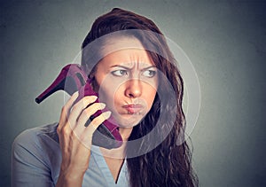 Upset woman holding high heeled shoe in her hand as phone