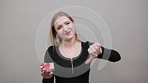 Upset woman holds gift Packed box in hand, thumbs down