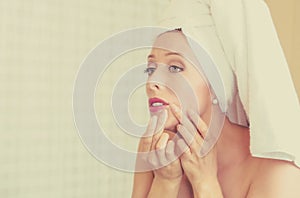 Upset woman looking in a mirror frustrated to see zit on her face, pimple photo