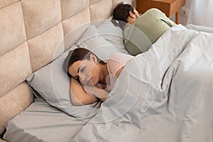 Upset woman lying in bed with back to man