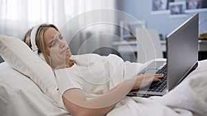 Upset woman lying in bed, disappointed with old laptop malfunction, service