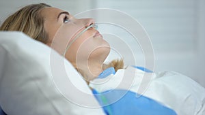 Upset woman lying with oxygen nasal catheter on face, preparation for surgery