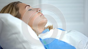Upset woman lying with oxygen nasal catheter on face, preparation for surgery