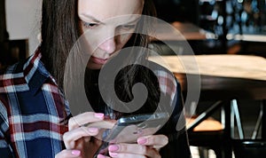 Upset woman sends a message or use internet in the phone sitting in a cafe. Dressed in a plaid shirt.