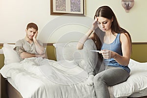 Upset woman sitting on bed and looking at pregnancy test