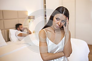 Upset Woman Sitting On The Bed With Man In The Background. Woman and man having a disagreement, Young couple in a bed bored woman