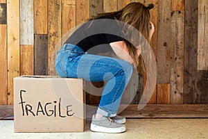 Upset Woman sitting on Floor with her cardboard moving box in her new home, tired and depression near wooden wall retro design