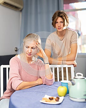 Upset woman sitting at home after disagreements with teenage son