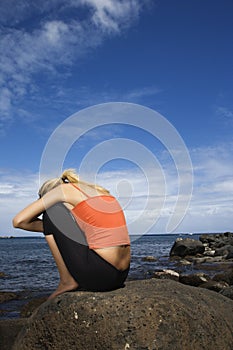 Upset woman sitting on rocky shore.