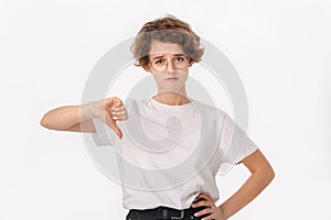 Upset woman in white shirt and eyeglasses holding thumb down to express negative attitude
