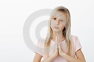 Upset worried little girl asking friend for forgiveness. Studio shot of sad cute daughter with fair hair in pink t-shirt