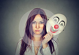 Upset worried woman with sad expression taking off clown mask