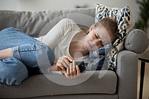 Upset worried young woman crying lying on couch holding phone