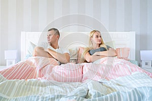 Upset young couple having marital problems or a disagreement sitting side by side in bed facing in opposite directions