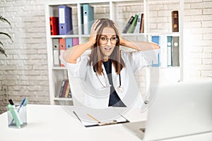 Upset young female doctor looking at laptop