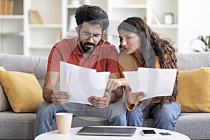 Upset Young Indian Couple Suffering Financial Crisis Checking Papers At Home