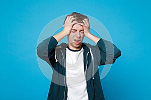 Upset young man in casual clothes screaming crying putting hands on head keeping eyes closed isolated on blue wall