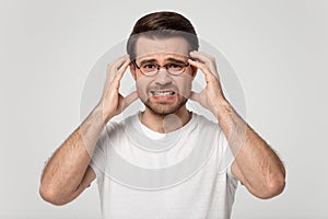 Upset young man in eyeglasses suffering from sudden strong headache.