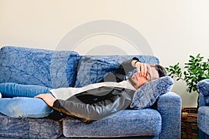 Upset young man lying on couch resting at home feeling fatigue, tired, suffer from migraine