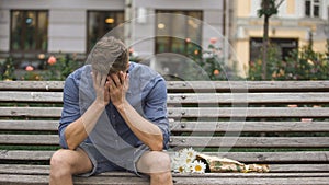 Upset young man sitting on bench alone, closing face with hands, break-up