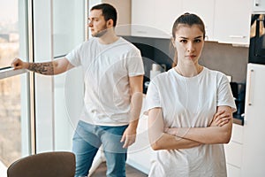 Upset young spouses standing, quarreling, apart in the kitchen