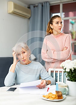 Upset young woman with aged mother looking worriedly at papers at home
