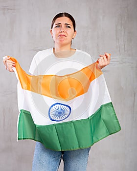 Upset young woman holding flag of India on gray wall background, sad expression