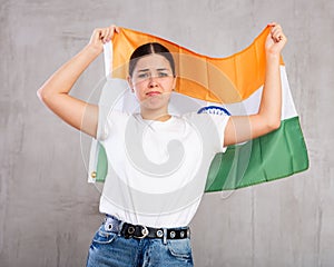 Upset young woman holding flag of India on gray wall background, sad expression