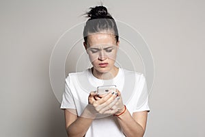 Upset young woman looks at her smartphone and frowns. She sees bad news or photos that cause her negative emotions