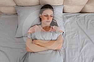 Upset young woman lying in bed, hugging pillow with a worried expression