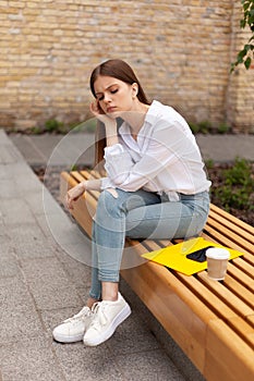 Upset young woman sits outdoors. Headache and burnout