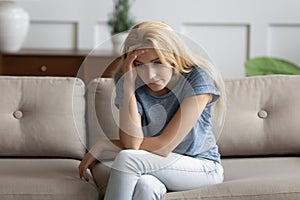 Upset young woman sitting on couch thinking about life troubles photo