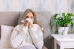 Upset young woman suffering from influenza at home. Female blows her nose holding tissue handkerchief, having symptoms
