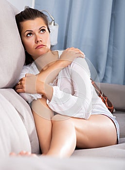 Upset young woman suffering from troubles on sofa in home iterior