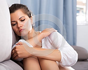 Upset young woman suffering from troubles on sofa in home iterior