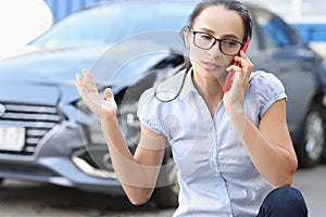 Upset young woman talking on phone against background of broken car