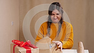 Upset young woman trying to wrap a gift in kraft paper tears her up in anger