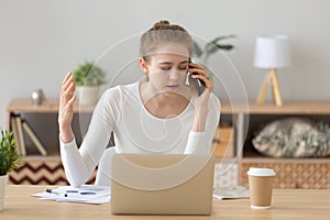 Upset female working ta laptop having unpleasant talk on phone photo