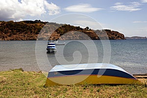 An upside down boat and fishing boats in the beach in the island of Patmos, Greece in summer time