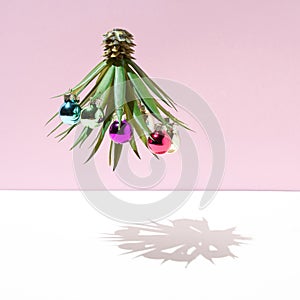 Upside down pineapple palm tree decorated with ornaments of balls of different colors and its shadow. Minimal Christmas concept on