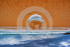 Upside-down shot of a crystal ball with the reflection of the sandy beach, sea and cloudy sky