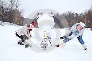 Upside down snowman and two women try to raise it photo