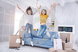 Cheerful young girls jumping happily in new apartment